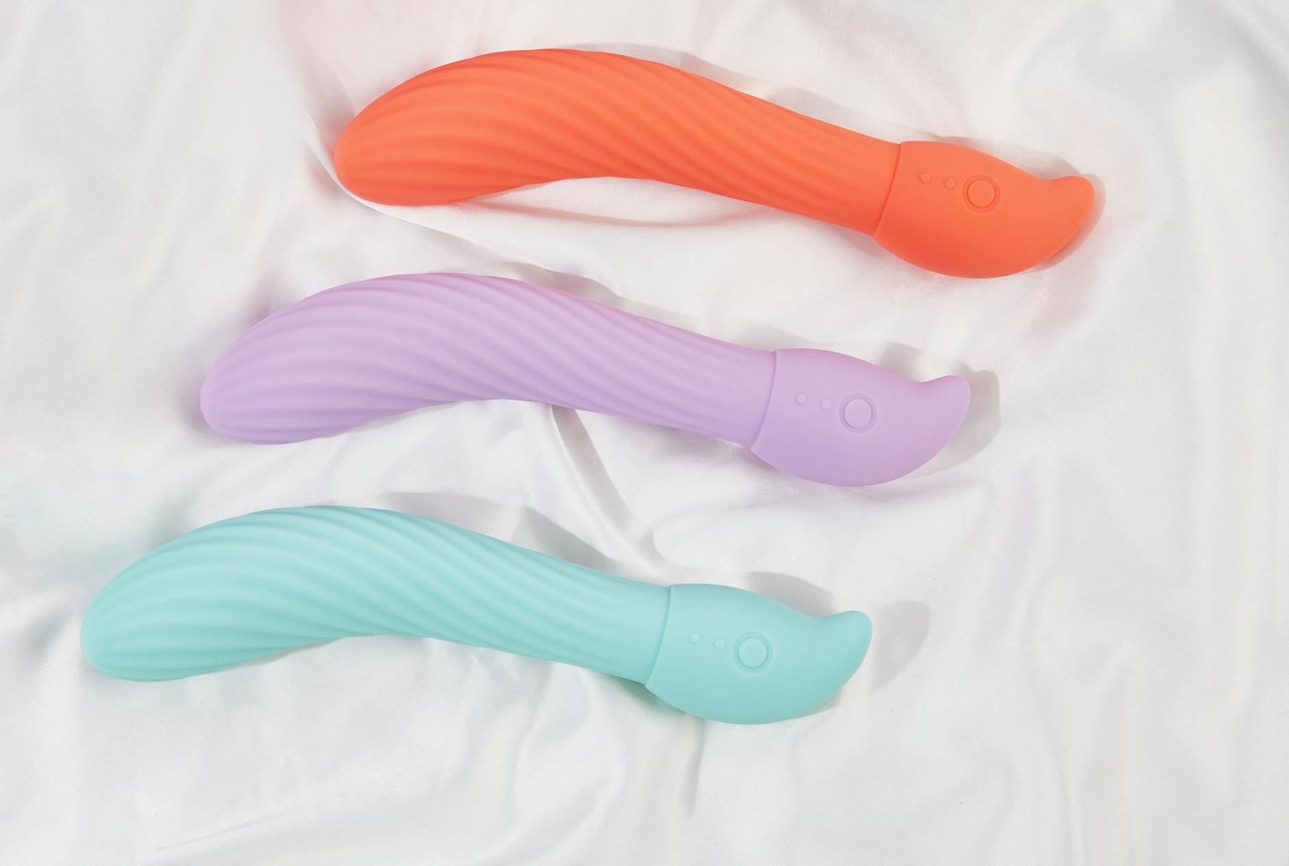 Tres vibradores coloridos dispuestos en tela blanca, destacando su textura suave y diseño ergonómico