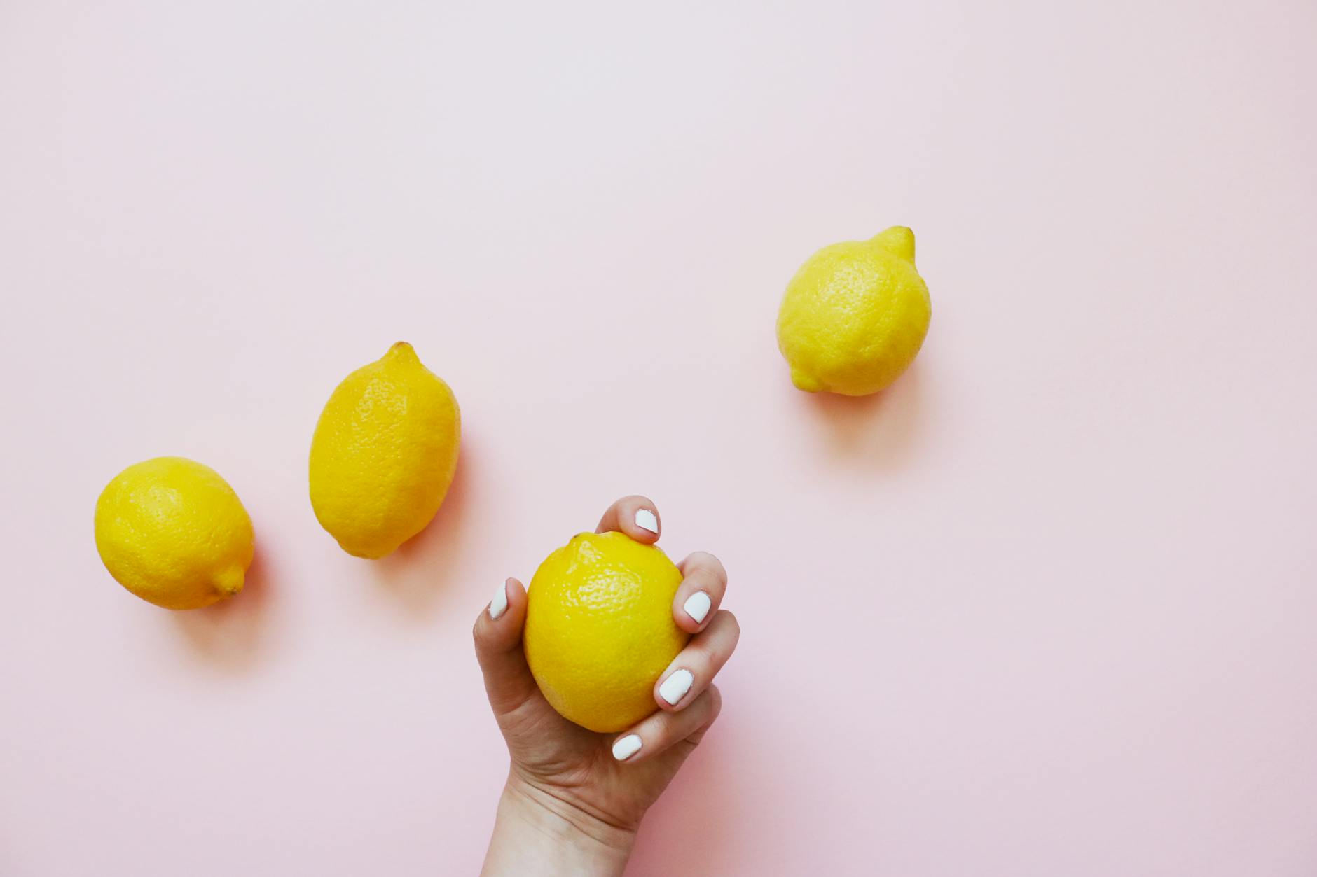 Mano sosteniendo un limón fresco sobre fondo rosa suave, simbolizando placer y renovación después de los 50