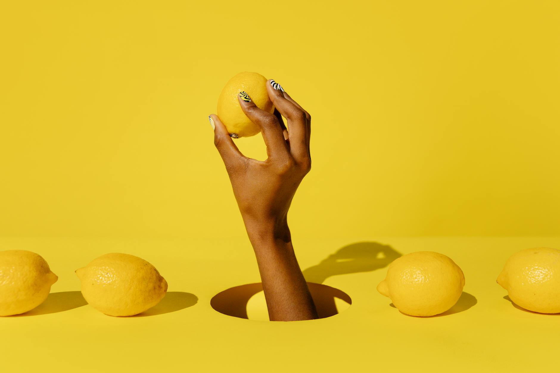 Mano sosteniendo un limón fresco contra fondo amarillo vivido, simbolizando cuidado y sensibilidad