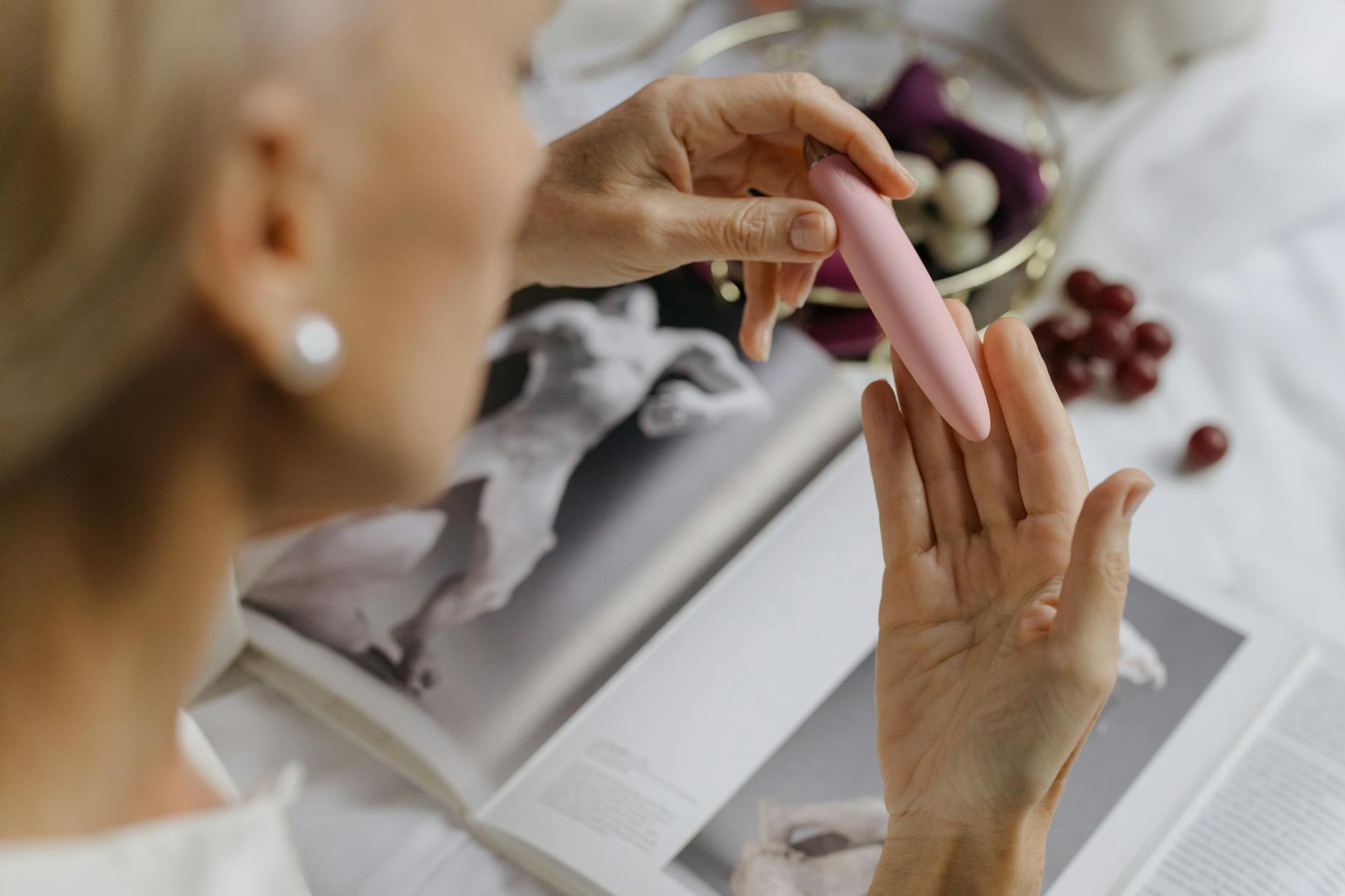 Mujer sosteniendo un vibrador rosa junto a libros de arte, simbolizando intimidad y placer personal consciente