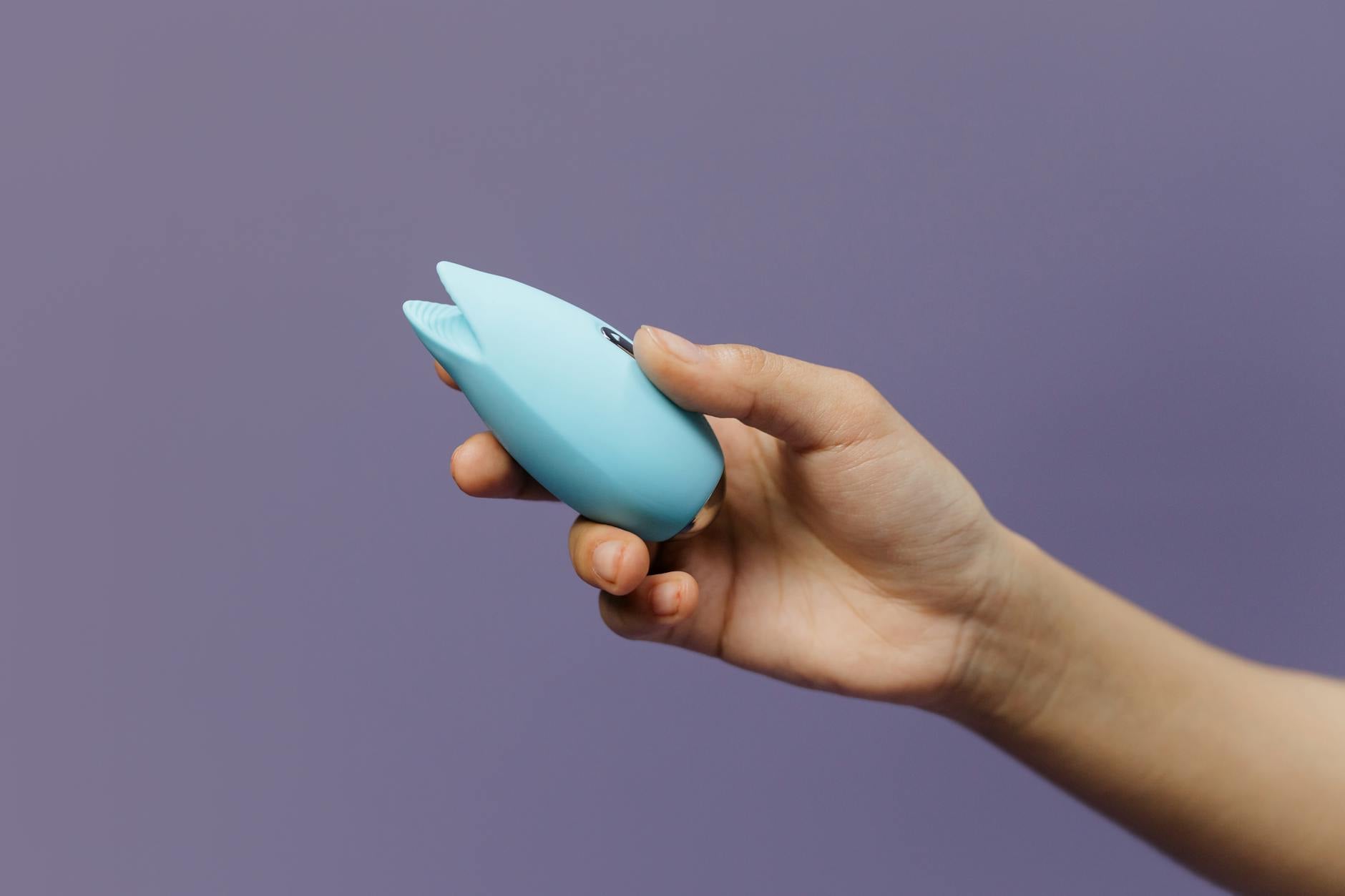 Vibrador azul de silicona sostenido en la mano contra fondo púrpura, promoviendo el auto-placer y la sexualidad