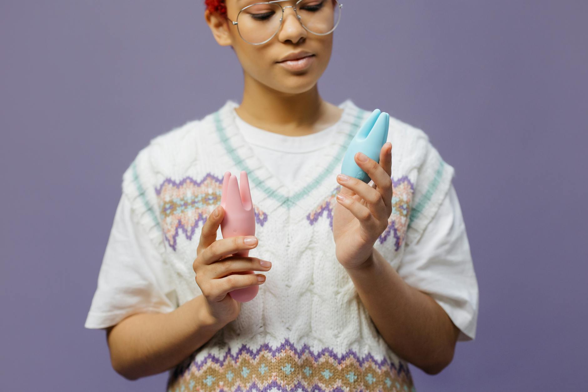 Persona sosteniendo un vibrador clitorideo azul y rosado con expresión reflexiva
