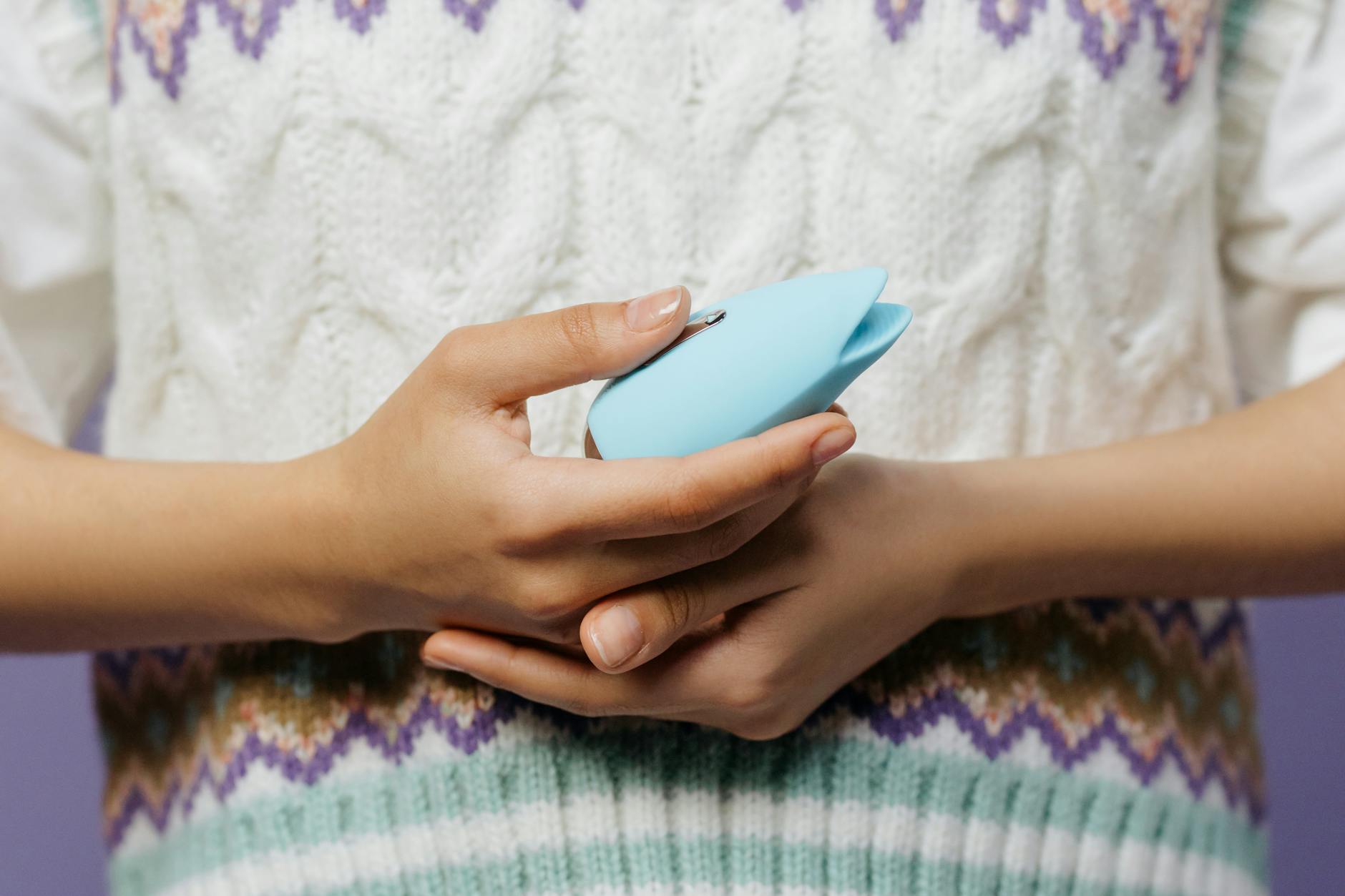 Manos sosteniendo un vibrador azul contra un suéter tejido